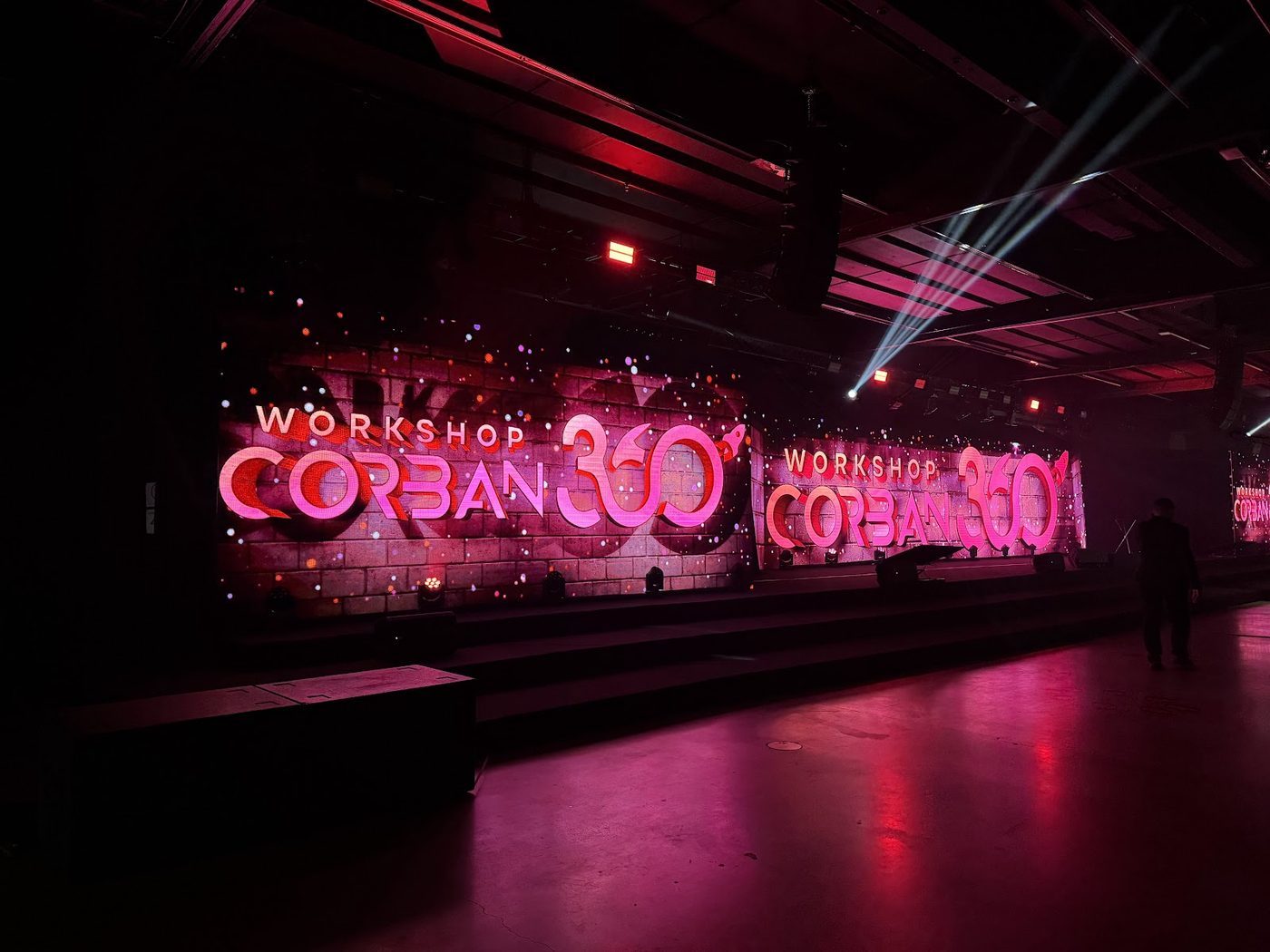 Congresso corporativo com painéis LED curvos, feixes de luz cênica e ambientação temática em tons rosa