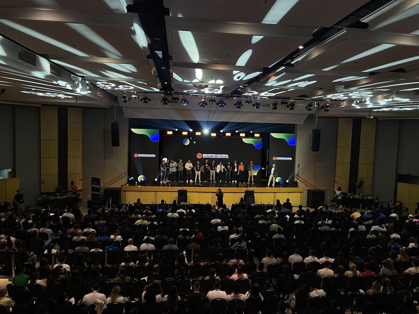 Congresso corporativo com palco, painel LED com logo do evento e plateia lotada
