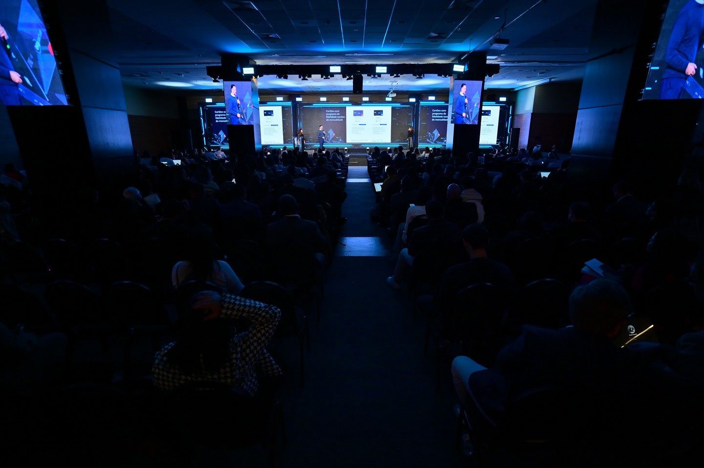 Auditório corporativo com câmeras IMAG e telões laterais amplificando imagem do palestrante no palco