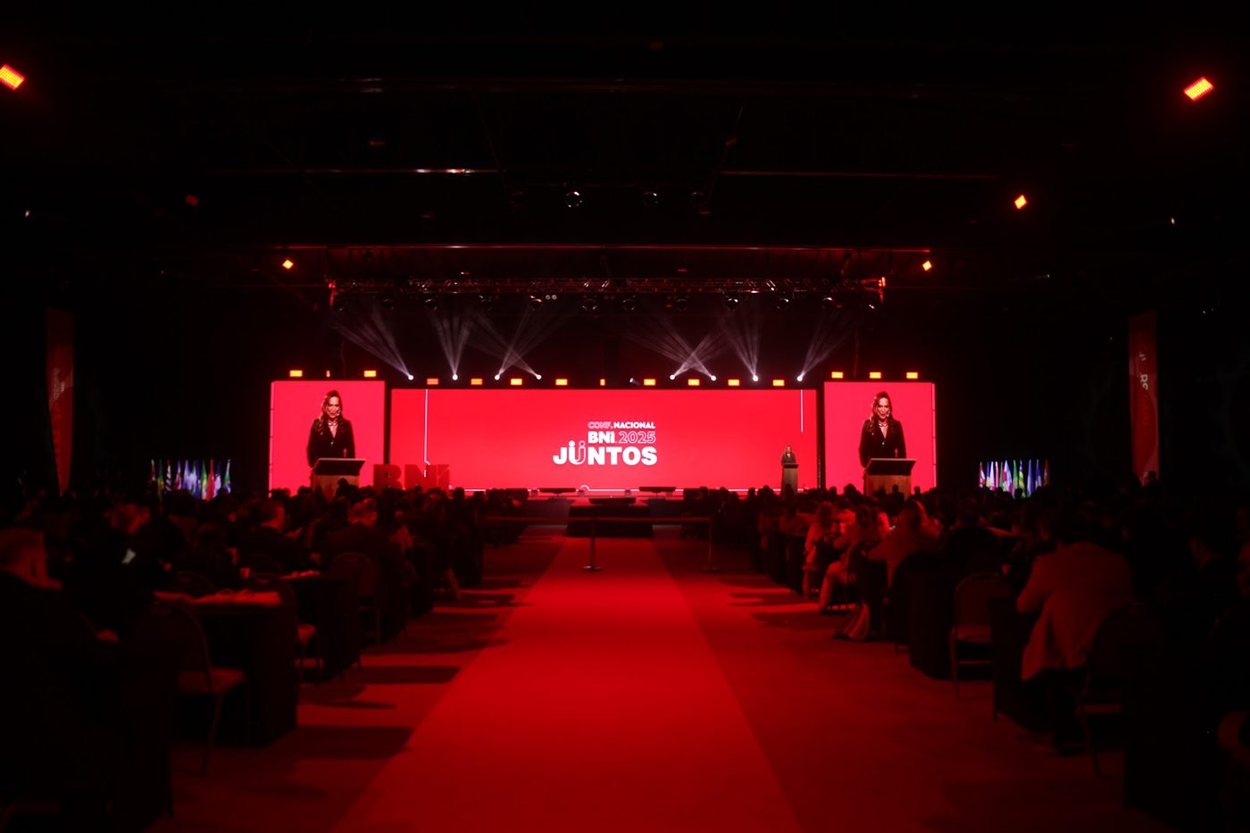 Palco de convenção BNI com painel LED vermelho e plateia sentada em auditório corporativo
