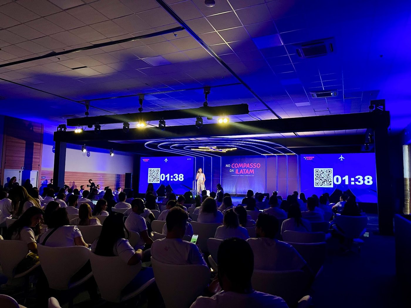 Auditório corporativo LATAM com painéis LED azuis e contagem regressiva na tela principal