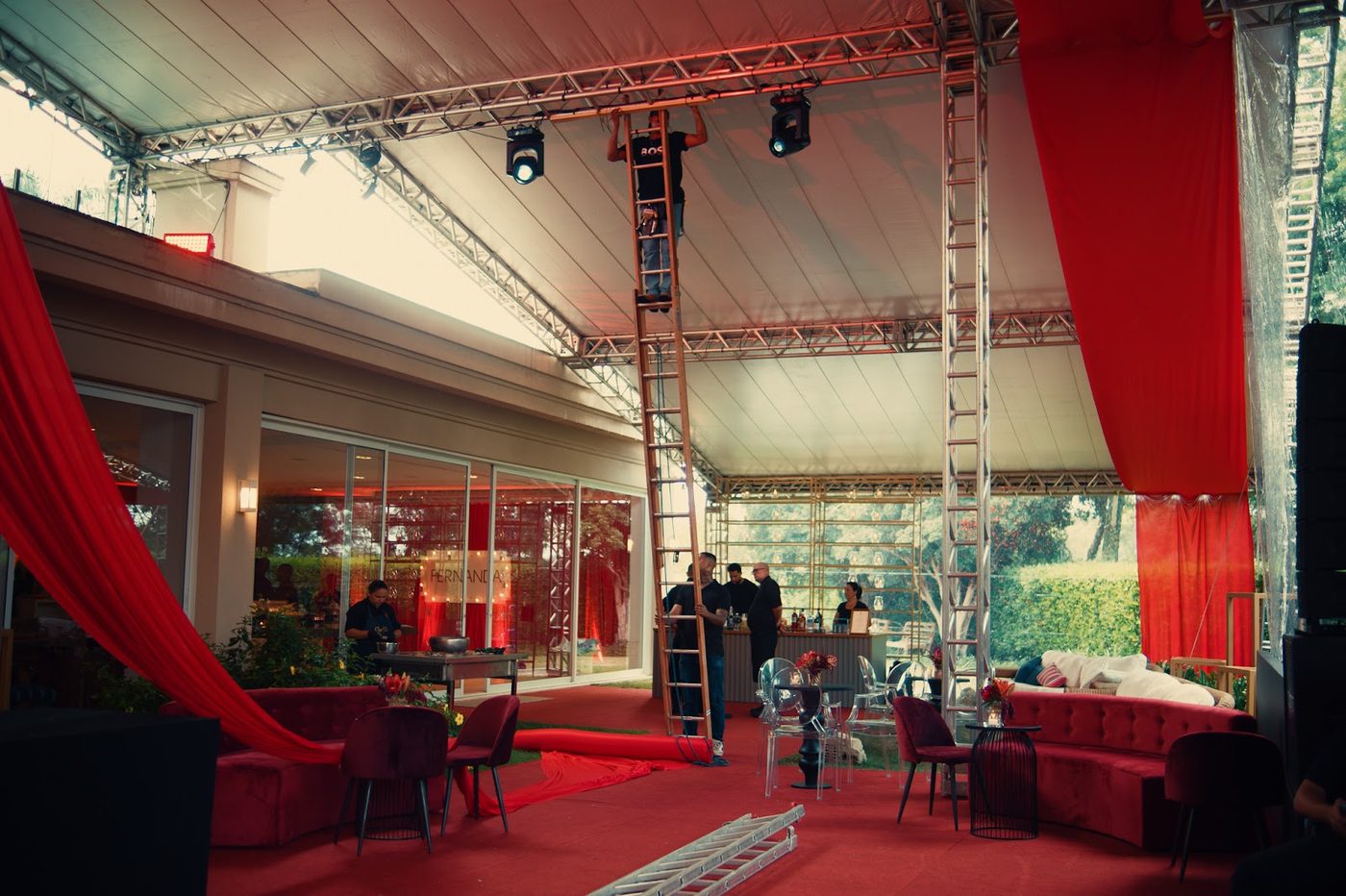 Técnico em escada fazendo rigging de refletores em treliça de alumínio durante montagem de evento