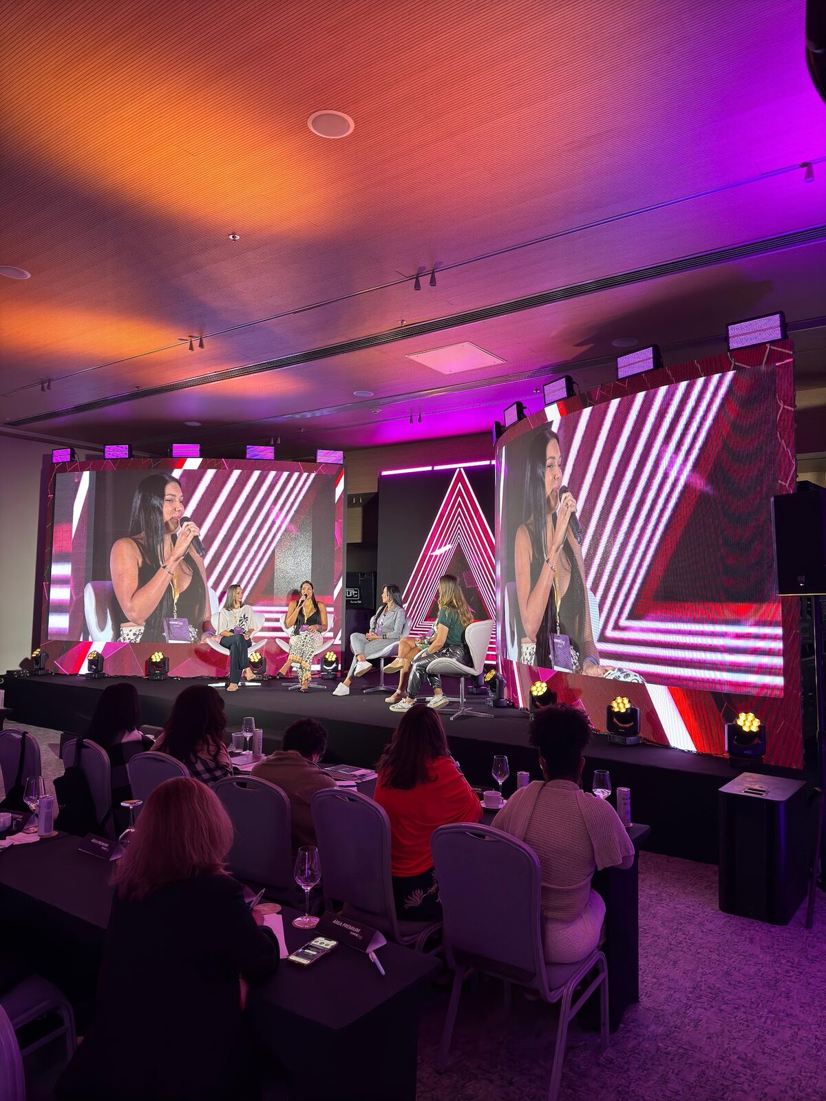 Mesa-redonda em evento corporativo com painéis de LED assimétricos em tons de rosa e roxo