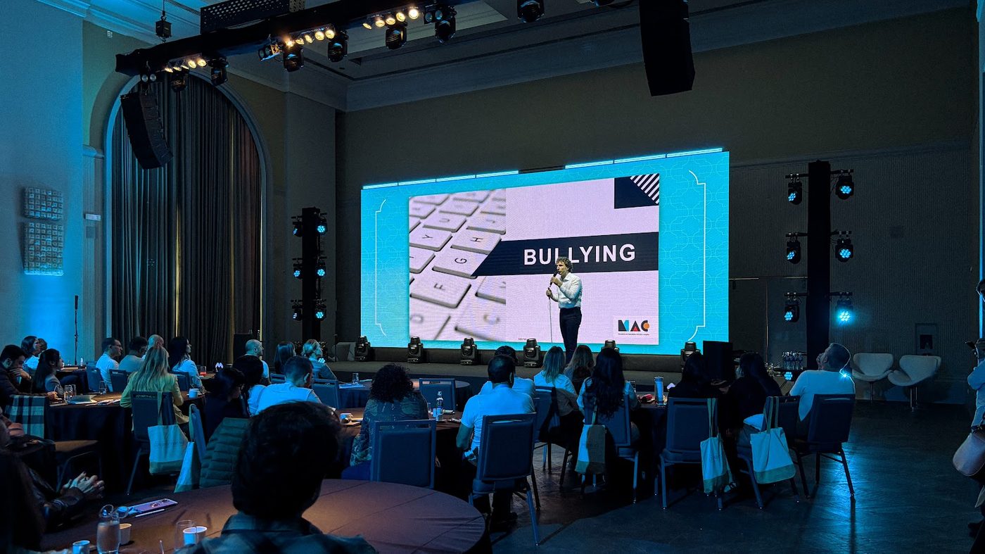 Palco corporativo com painel LED, caixas de som suspensas e plateia em mesas redondas em convenção corporativa