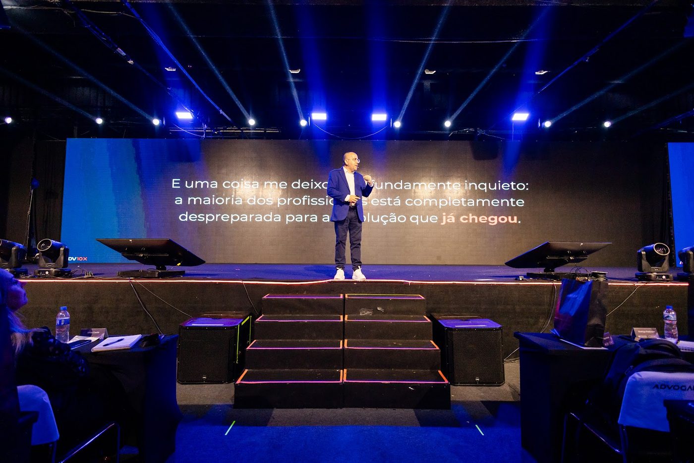 Palestrante no palco com telão LED e caixas de som em evento corporativo