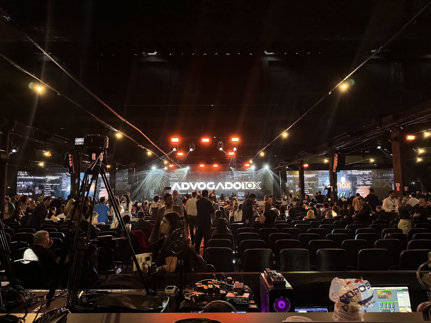 Plateia em pé em evento corporativo com iluminação cênica e câmeras de transmissão ao vivo