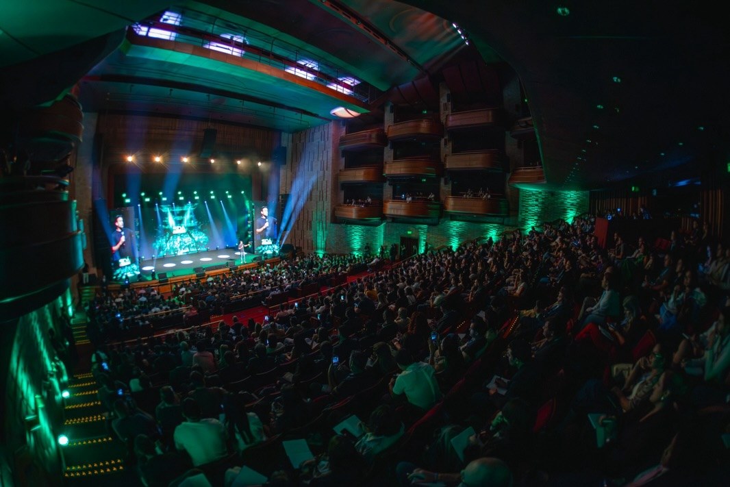 Plateia lotada no Teatro Bradesco durante o SDA 2026, com telas de LED, feixes de luz e iluminação verde nas laterais