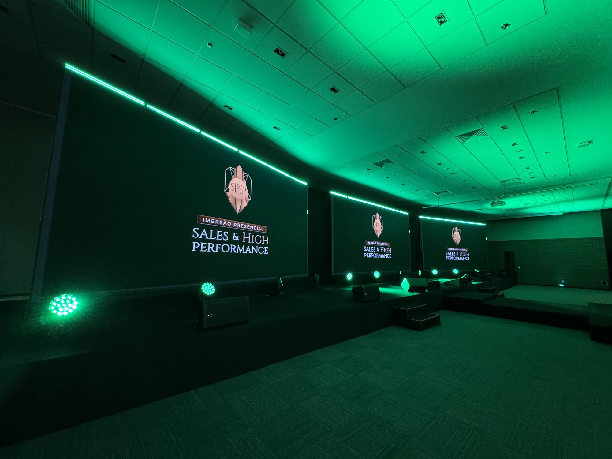 Palco do SHP 2025 com três painéis de LED em leque e iluminação verde no Blue Tree Alphaville