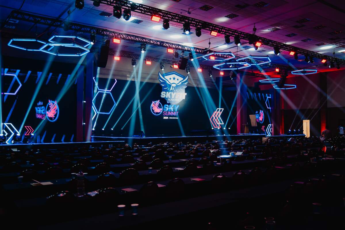 Palco de evento corporativo com estruturas hexagonais em neon, treliça de luz e painel de LED integrados à cenografia