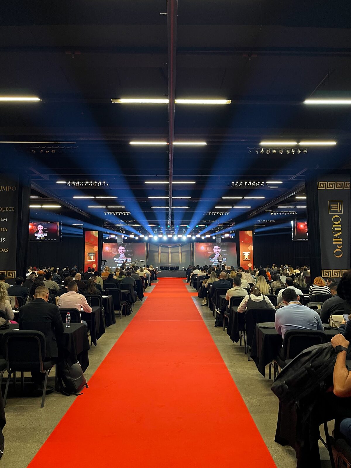Plateia lotada em evento corporativo com telões de LED e iluminação cênica ao fundo