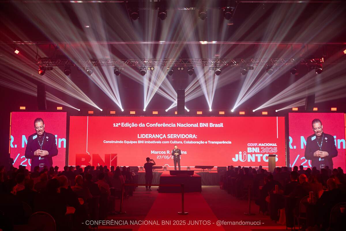 Palco de conferência com painéis de LED em tela cheia, treliça e feixes de luz em evento corporativo