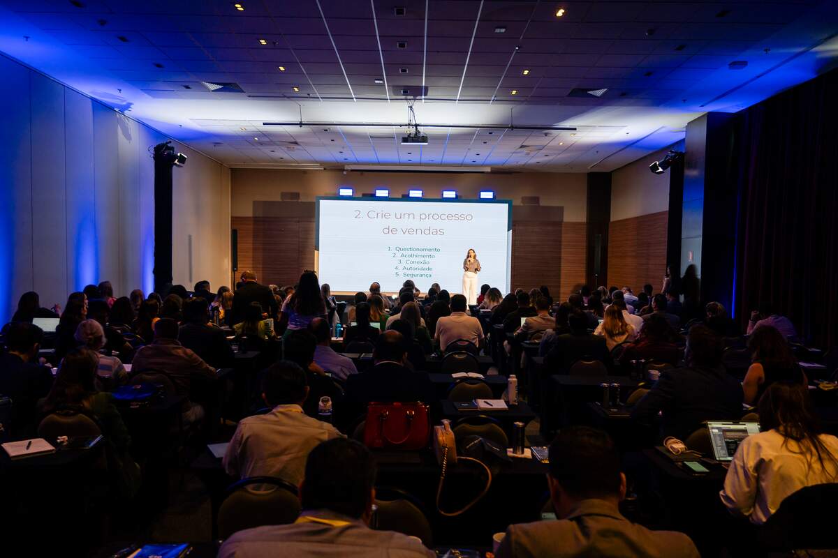 Auditório de evento corporativo com plateia diante do telão de apresentação