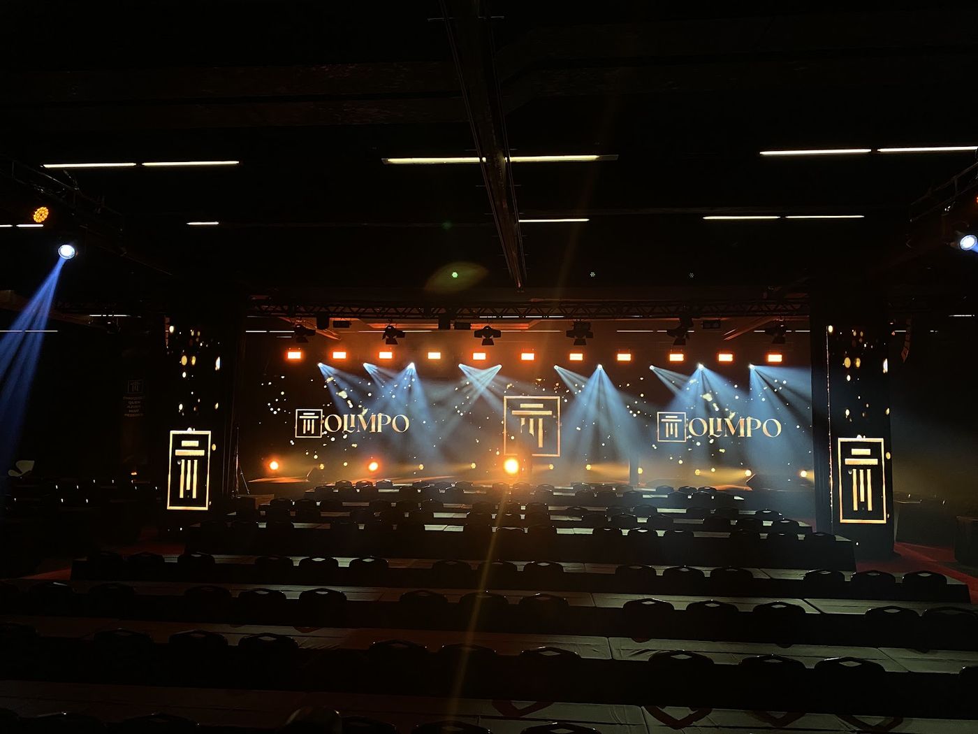 Feixes de luz simétricos convergindo sobre palco de convenção corporativa com painel LED