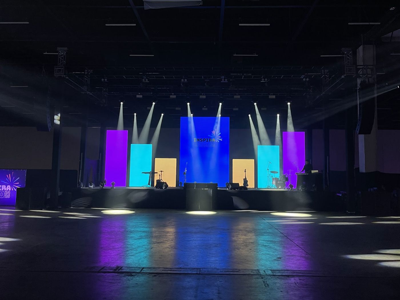 Palco corporativo com treliça e feixes de luz cênica coloridos realçados por haze em evento