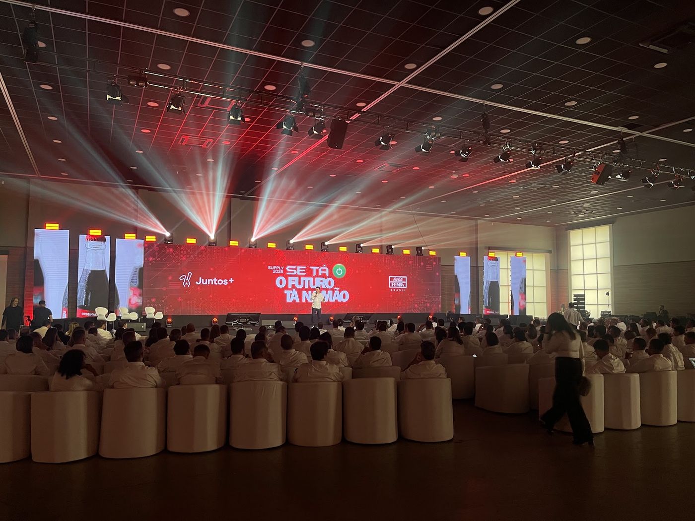 Plateia de convenção corporativa sob feixes de luz cênica com painel LED vermelho ao fundo