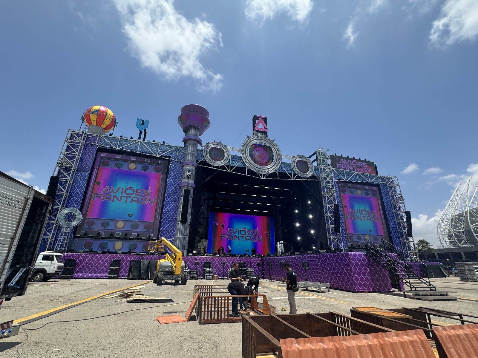 Palco ao ar livre em dia de sol com painéis de LED e estrutura de treliça sendo montado pela equipe da Showdesign