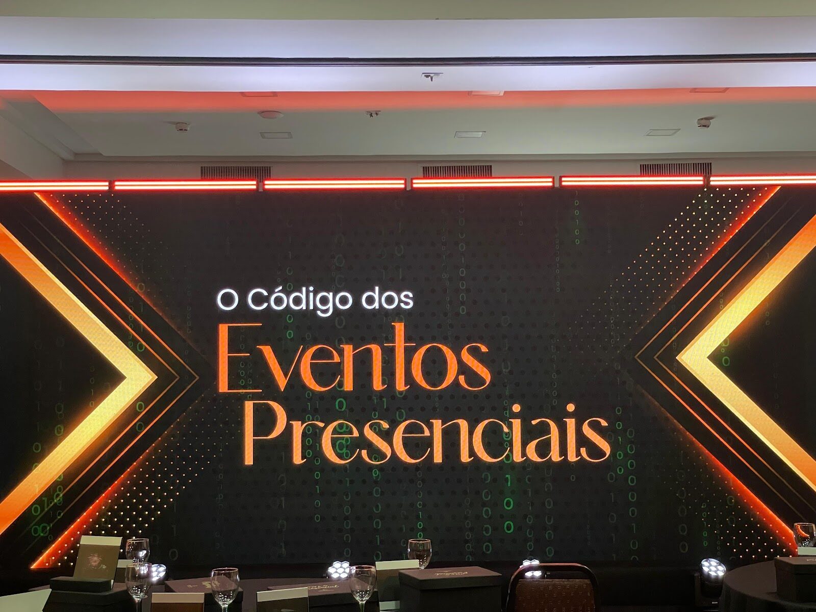 Painel de LED de alta resolução com arte em laranja e preto atrás da mesa de palestrantes de evento corporativo