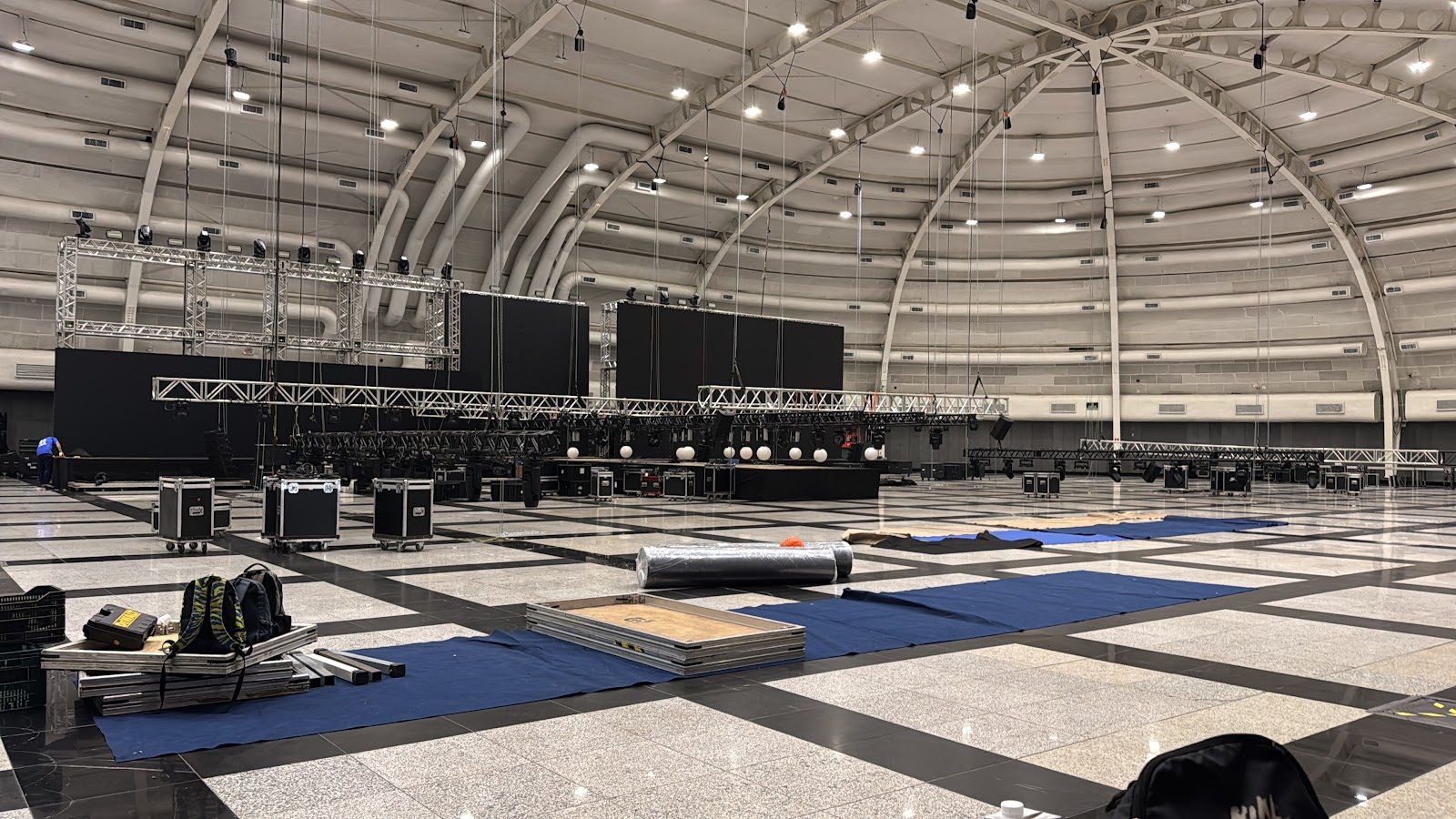 Montagem de convenção em pavilhão com talhas suspensas no teto, treliças e painéis de LED no chão antes do içamento