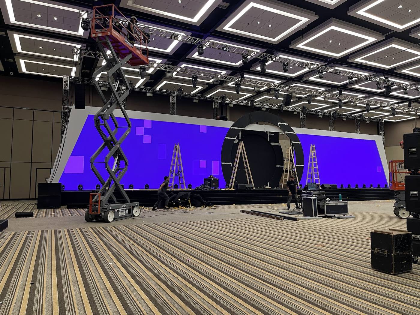 Equipe instalando painel de LED sob treliça com plataforma elevatória em centro de convenções