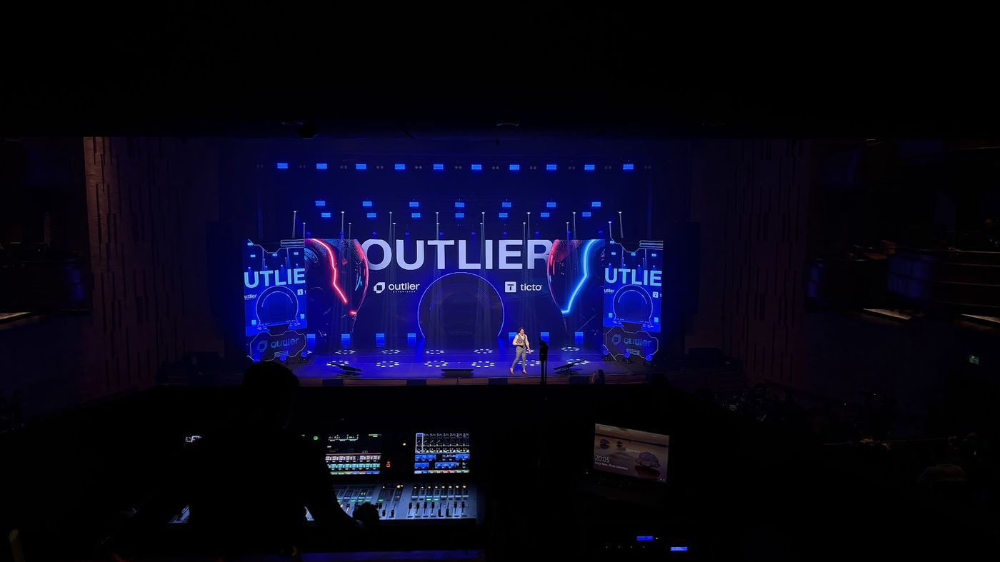 Palco corporativo com painel LED visto da mesa de controle técnico ao fundo
